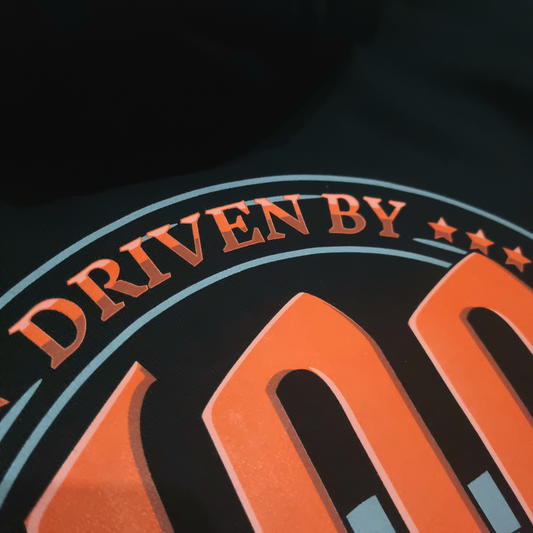 Black oversized box-fit premium hoodie with 'DRIVEN BY CHAOS' printed in large red letters within a car steering wheel on the back.