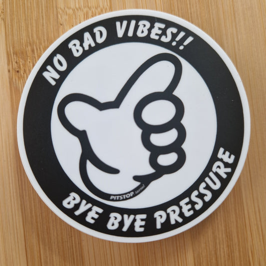 Circular sticker with a thumbs up icon and text 'No bad vibes!! Bye bye pressure' on a wooden surface.