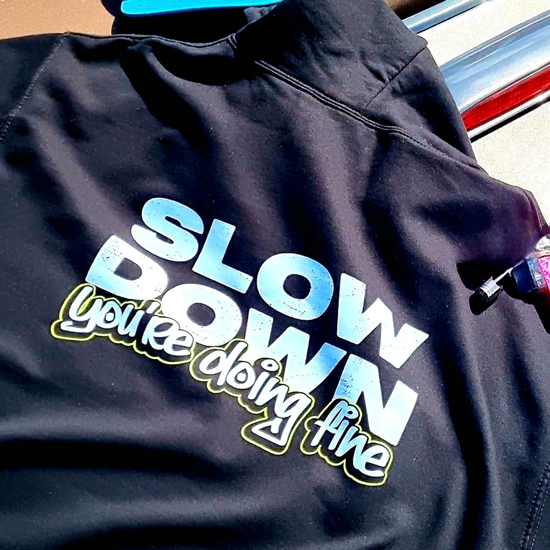 Black hoodie with the text 'SLOW DOWN You're doing fine' printed on the back in graffiti text with green outline resting on the back of a galaxy grey mazda mx5