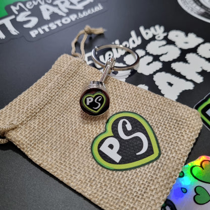Natural gift bag with PITSTOP.Social logo and green heart on a solid metal piston key chain fidget 