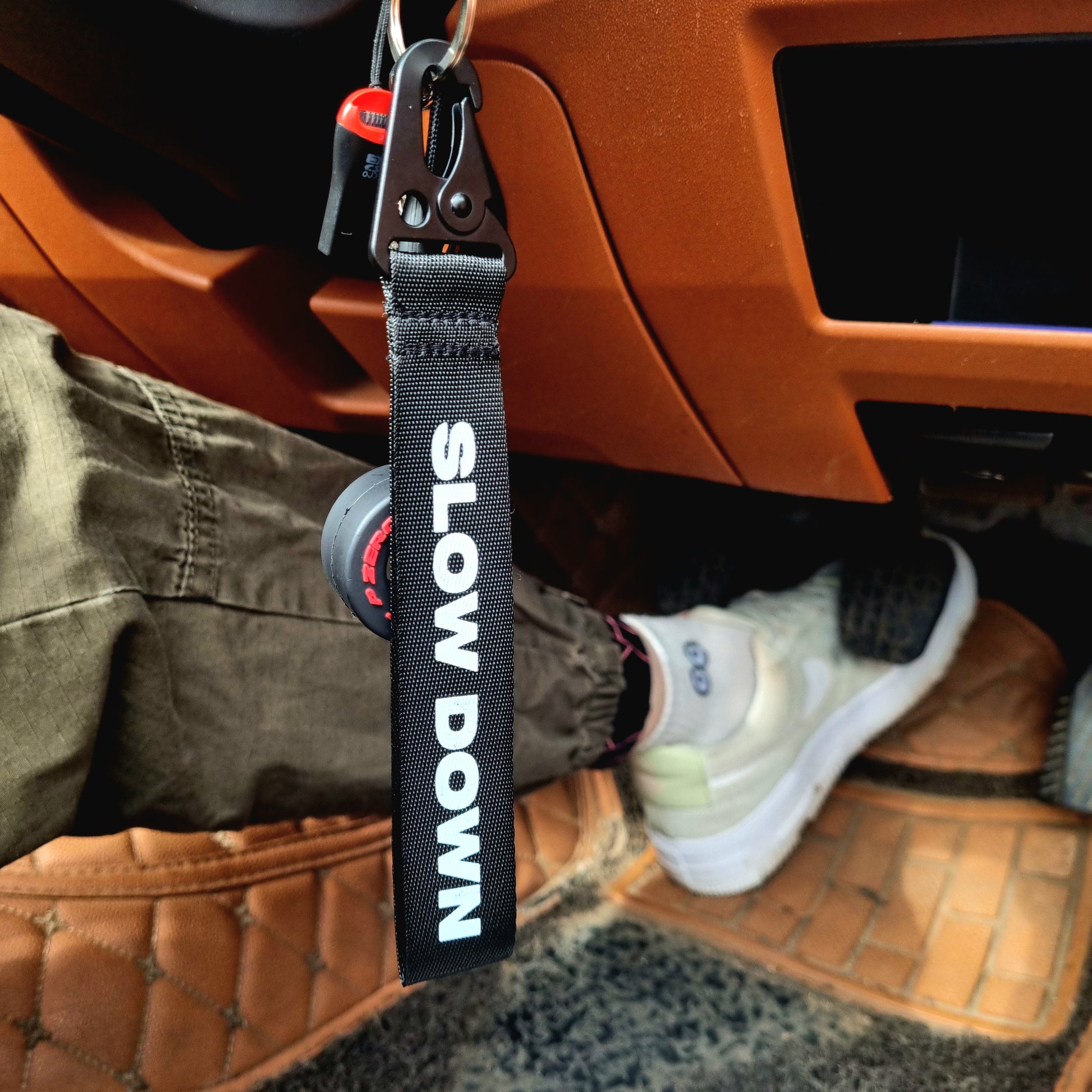 A black key tag with the text 'SLOW DOWN You're Doing Fine' in bold lettering, attached to a metal keychain ring inside Option Pack MAZDA mx5