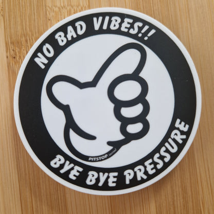 Circular sticker with a thumbs up icon and text 'No bad vibes!! Bye bye pressure' on a wooden surface.