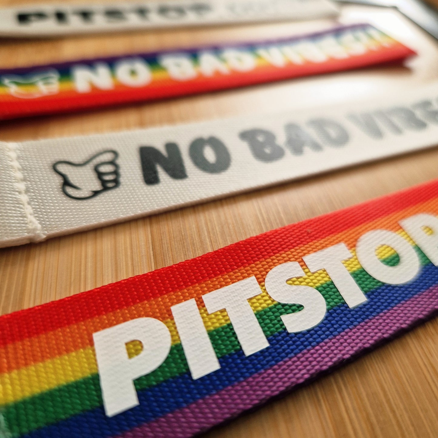 PITSTOP.Social branded rainbow strap with 'No Bad Vibes' text on a wooden surface