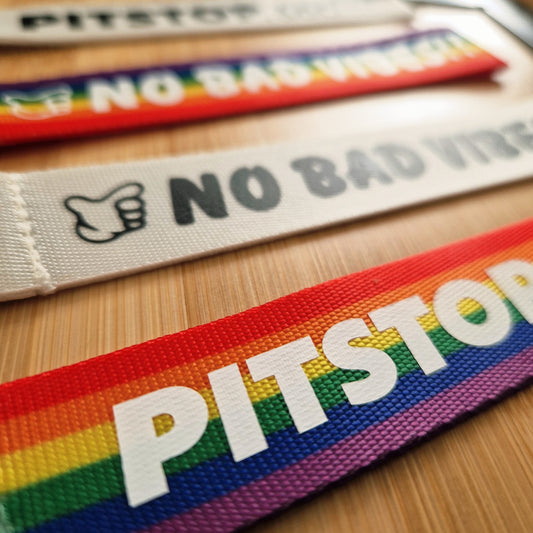 PITSTOP.Social branded rainbow strap with 'No Bad Vibes' text on a wooden surface