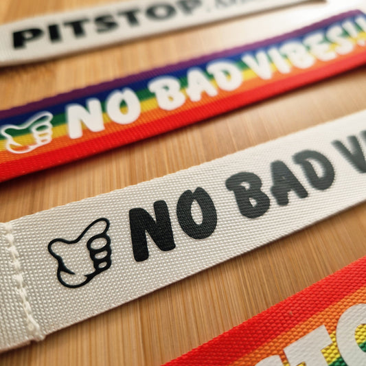 Rainbow woven keytag with 'NO BAD VIBES' text on a wooden surface