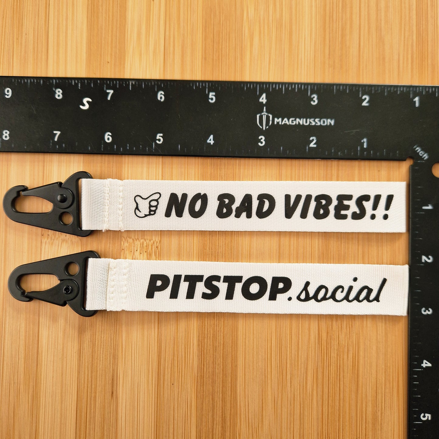 White woven keytag with 'NO BAD VIBES' text on a wooden surface