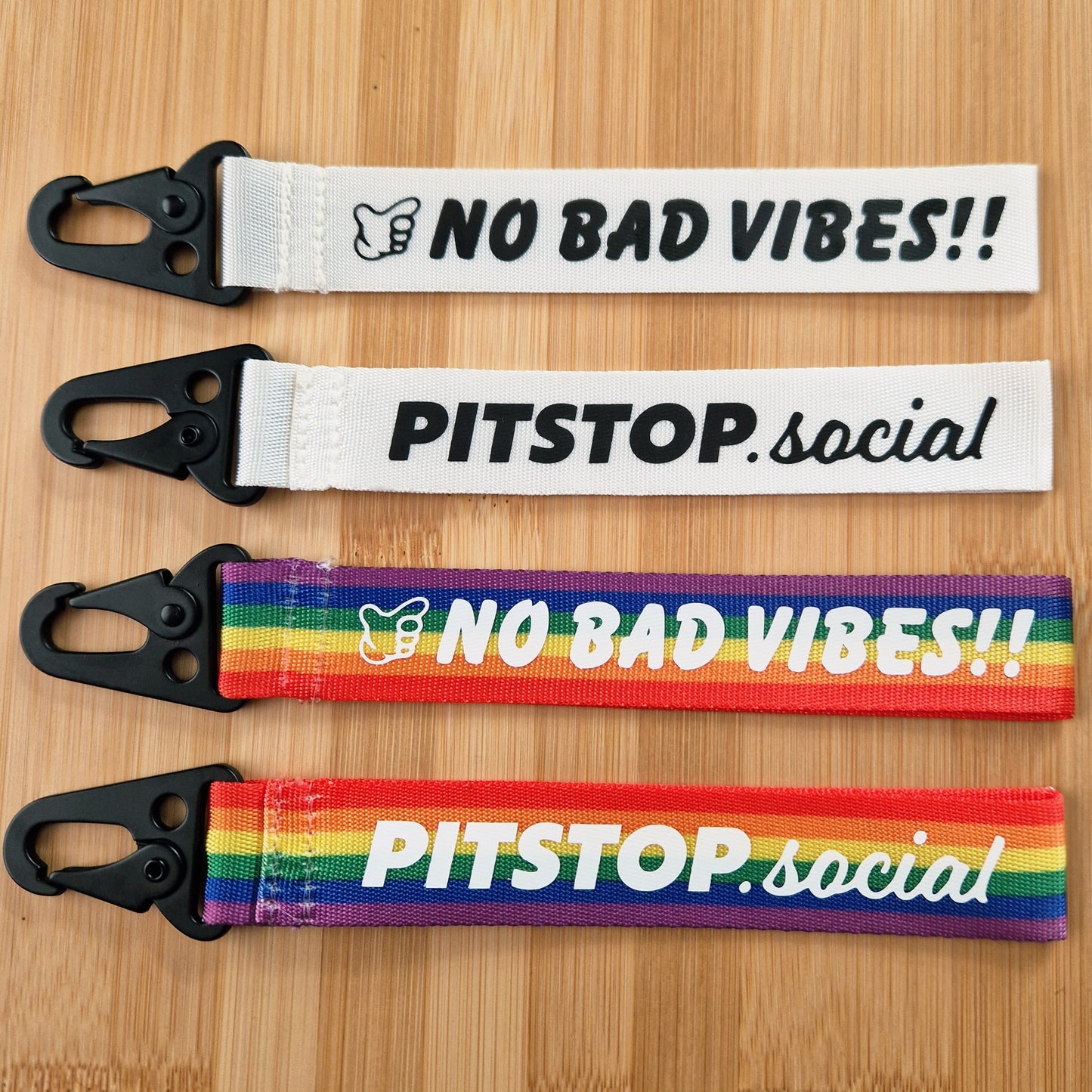 Rainbow and white woven keytag with 'NO BAD VIBES' text on a wooden surface