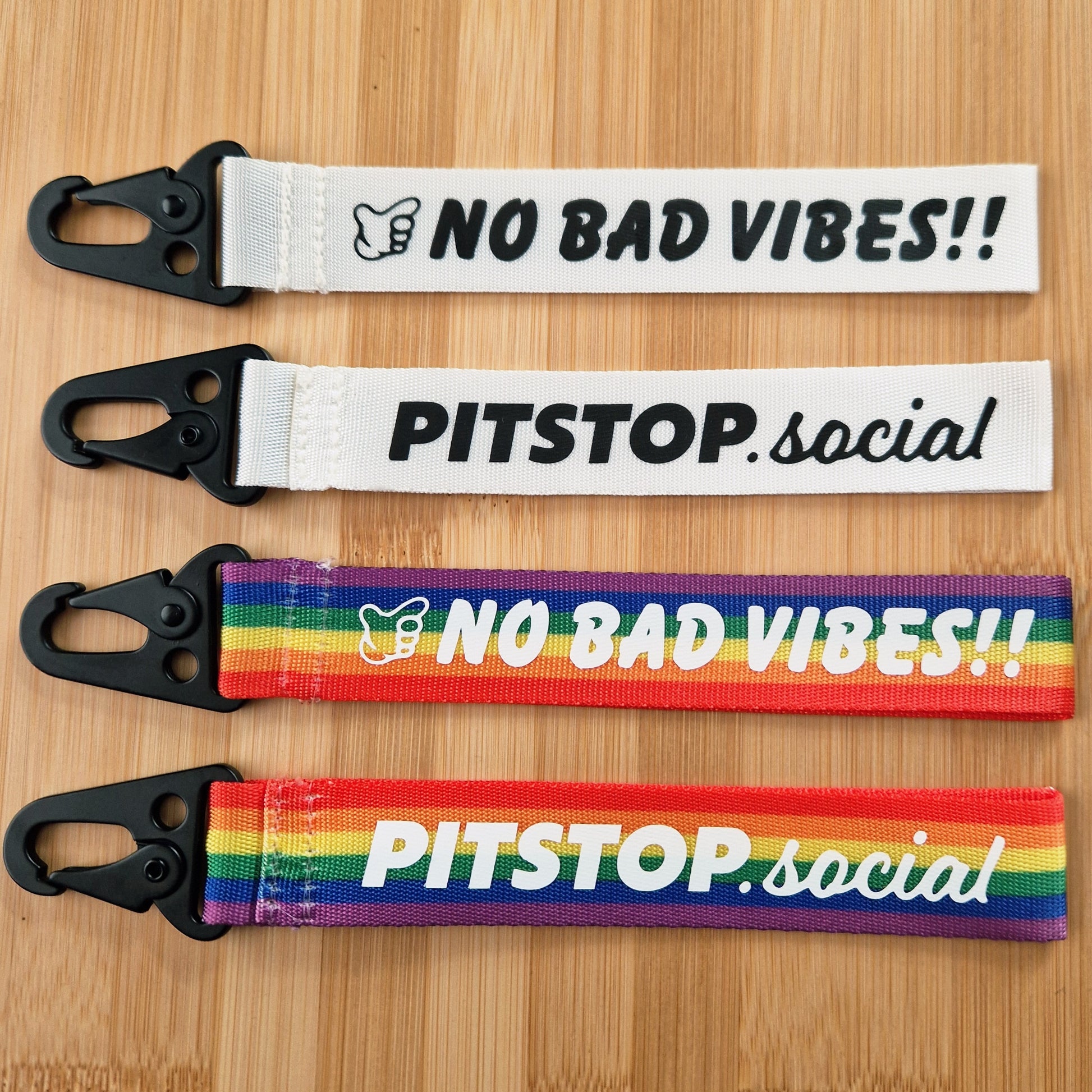 Rainbow and white woven keytag with 'NO BAD VIBES' text on a wooden surface