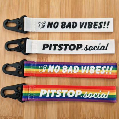 Rainbow and white woven keytag with 'NO BAD VIBES' text on a wooden surface