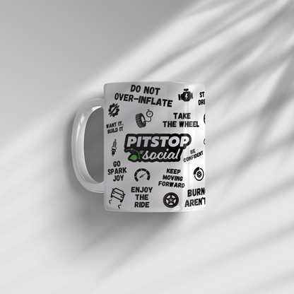 A white ceramic mug with 3D raised text and graphics including the Pitstop Social logo, various symbols of automotive relation, sunlight coming through onto plain white background.