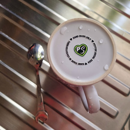 A white ceramic mug with 3D raised text and graphics including the Pitstop Social logo and text "hand made in Leicestershire" placed on a kitchen draining board.
