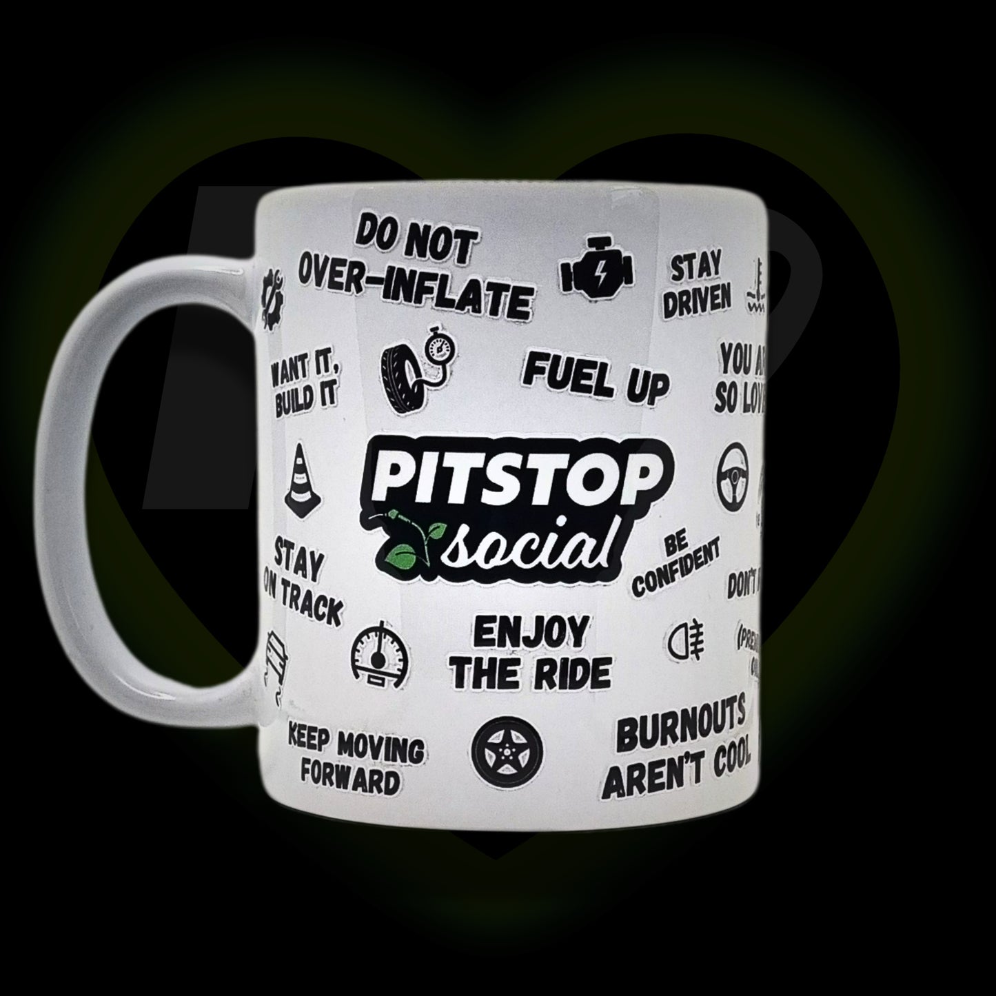 A white ceramic mug with 3D raised text and graphics including the Pitstop Social logo, various symbols, and a yellow lid with a spoon in it, placed on a wooden surface.
