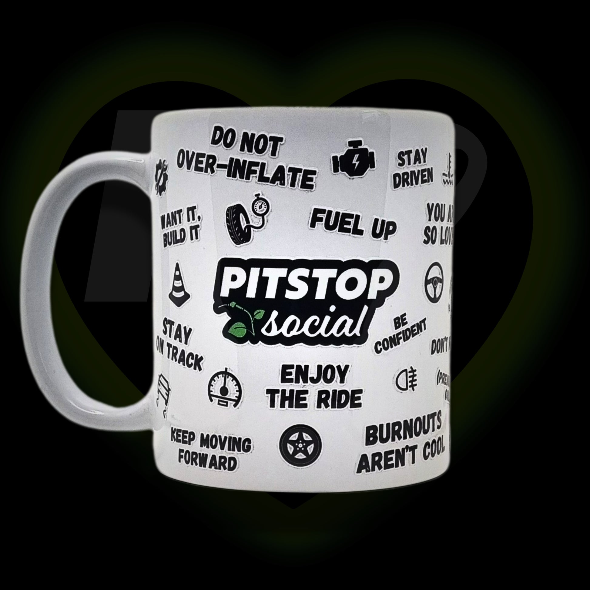 A white ceramic mug with 3D raised text and graphics including the Pitstop Social logo, various symbols, and a yellow lid with a spoon in it, placed on a wooden surface.