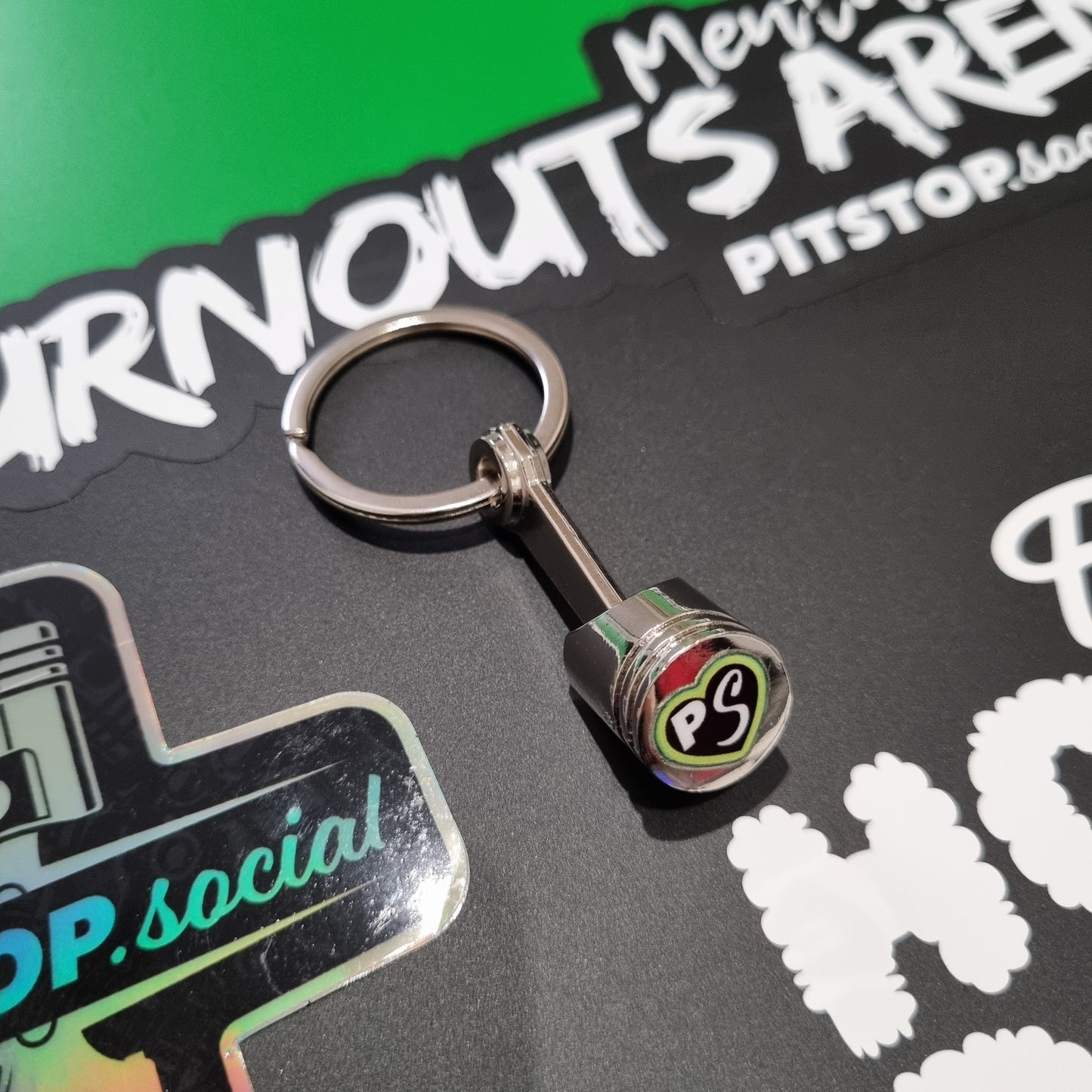 PITSTOP.Social logo green heart on a solid metal piston key chain fidget toy on a graffiti background