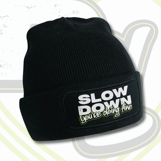 Soft black beanie hat with patch on front with graffiti text that says "SLOW DOWN you're doing fine"
